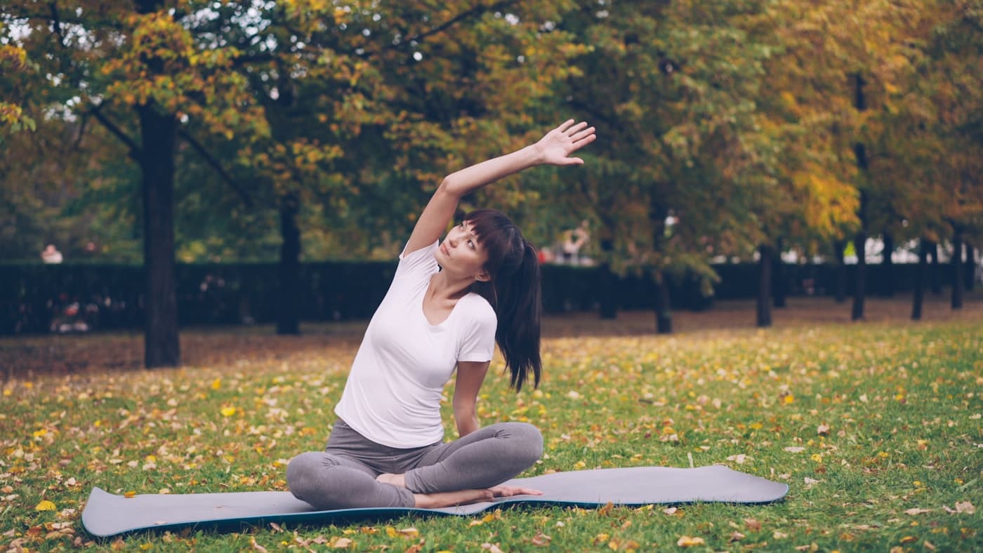 Mulher alongando em um tapete de yoga em um parque, em ritmo tranquilo